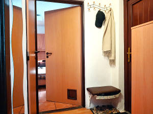 Předsíň se sedátkem, věšákem a botníkem. Pootevřenými dveřmi průhled do ložnice.